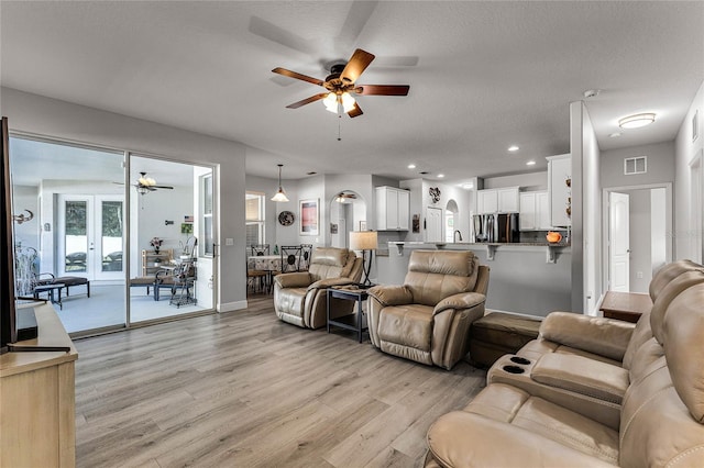 living room featuring arched walkways, visible vents, light wood-style flooring, and recessed lighting