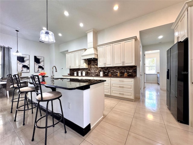 kitchen featuring sink, backsplash, hanging light fixtures, premium range hood, and a kitchen island with sink