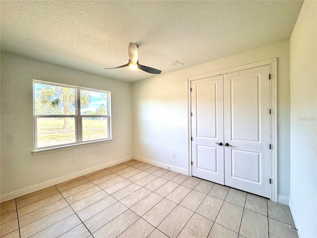 unfurnished bedroom with a textured ceiling, a closet, light tile patterned floors, and ceiling fan