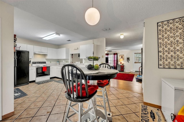 kitchen with white cabinetry, black fridge, white electric range, and light tile patterned floors