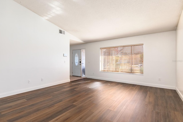 empty room with a textured ceiling, dark hardwood / wood-style floors, and vaulted ceiling