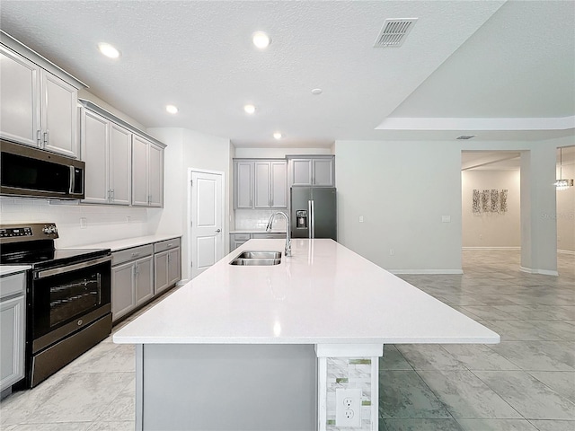 kitchen with appliances with stainless steel finishes, gray cabinetry, an island with sink, and sink