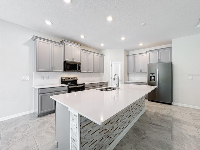 kitchen with appliances with stainless steel finishes, gray cabinetry, a kitchen island with sink, a breakfast bar, and sink