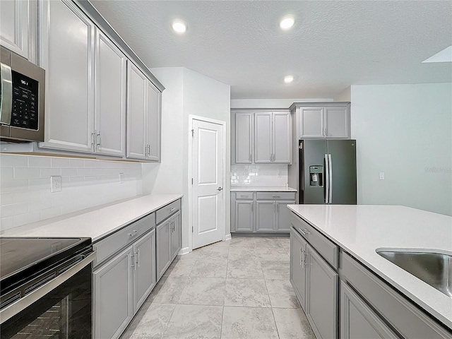 kitchen with a textured ceiling, appliances with stainless steel finishes, decorative backsplash, and gray cabinets