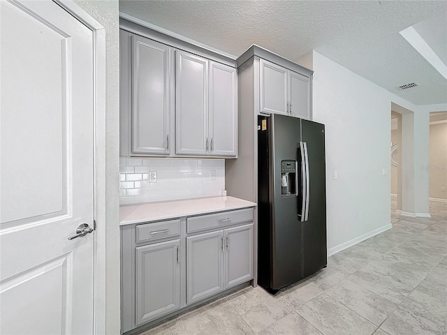 kitchen featuring backsplash, gray cabinets, a textured ceiling, and refrigerator with ice dispenser