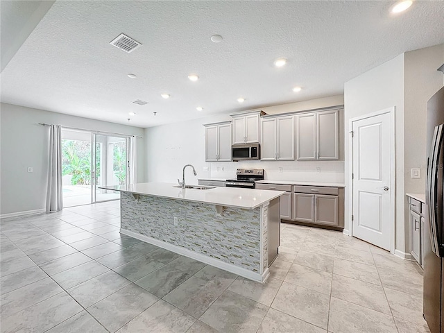 kitchen with light tile patterned floors, appliances with stainless steel finishes, an island with sink, and sink