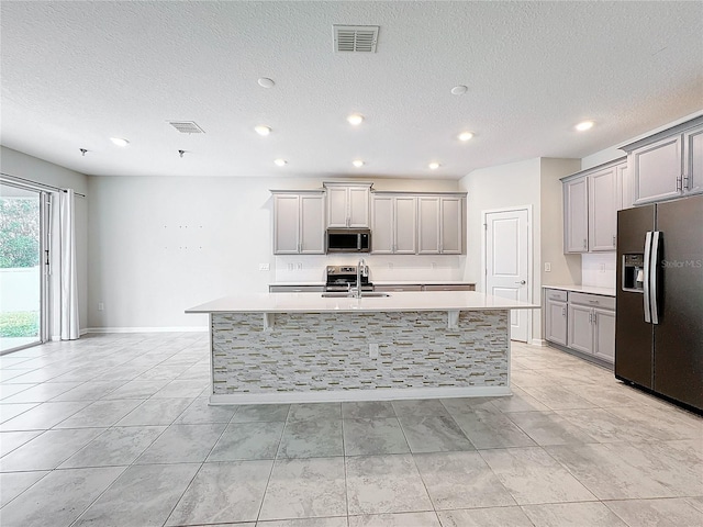 kitchen featuring a kitchen island with sink, appliances with stainless steel finishes, sink, and gray cabinetry