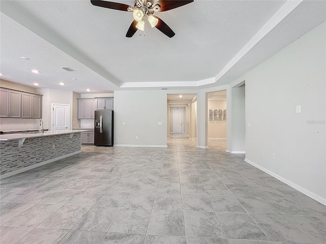 unfurnished living room with ceiling fan, sink, and a tray ceiling