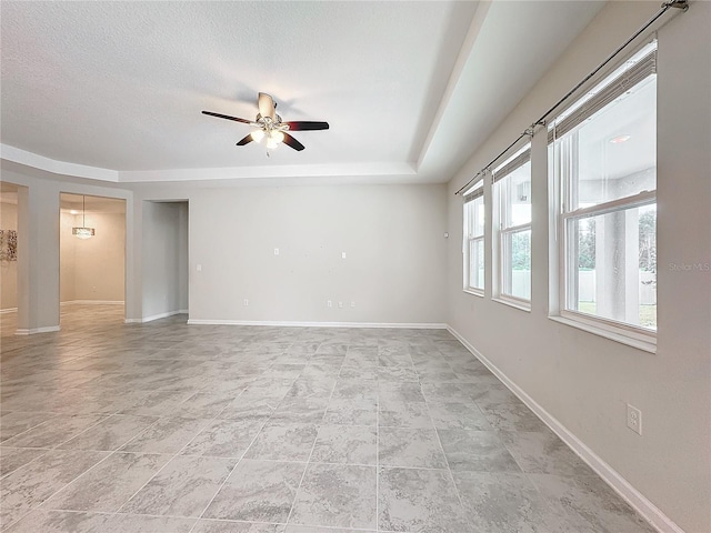 empty room featuring ceiling fan, a textured ceiling, and a tray ceiling