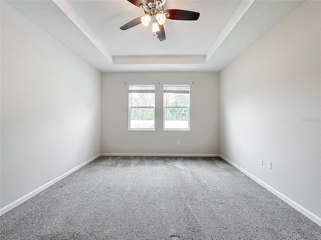 spare room with ceiling fan, a raised ceiling, and carpet flooring