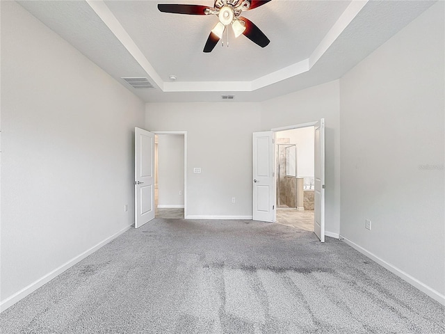 unfurnished bedroom with ceiling fan, connected bathroom, a raised ceiling, and light carpet