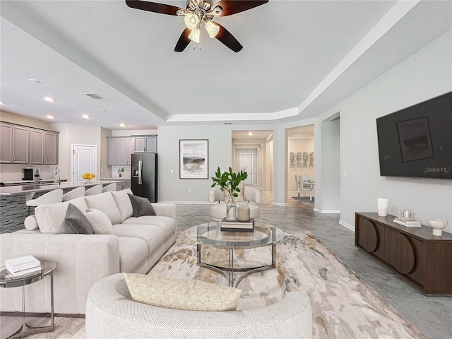 living room with a textured ceiling, ceiling fan, a raised ceiling, and sink