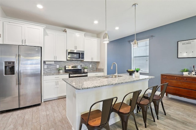 kitchen with a kitchen island with sink, appliances with stainless steel finishes, hanging light fixtures, and sink