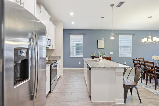 kitchen with white cabinets, a kitchen island with sink, stainless steel appliances, sink, and decorative light fixtures