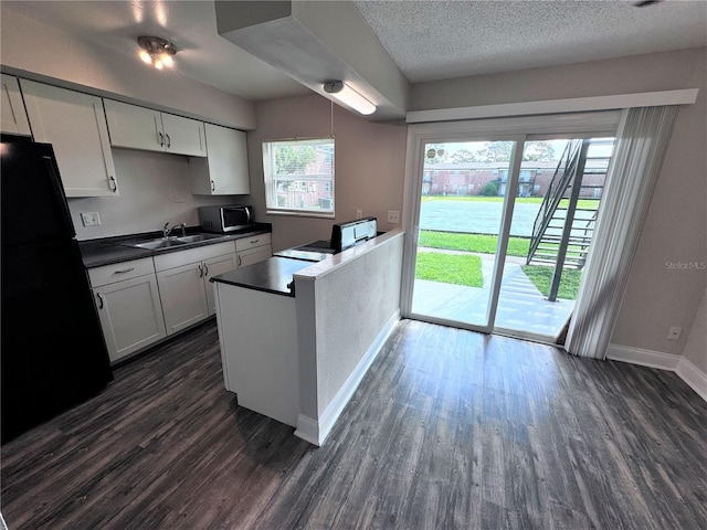 kitchen with black refrigerator, sink, dark hardwood / wood-style floors, white cabinetry, and hanging light fixtures