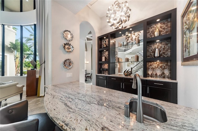 bar with sink, light stone counters, pendant lighting, a chandelier, and light wood-type flooring