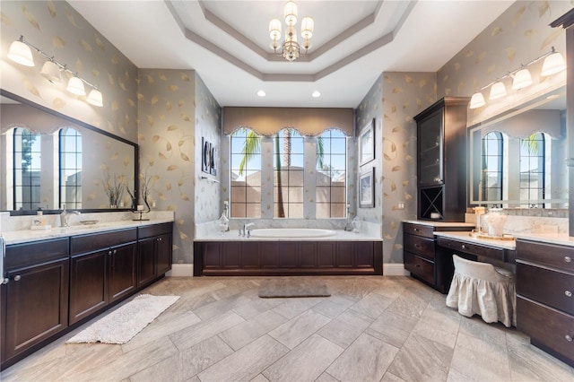 bathroom with a tray ceiling, a tub to relax in, vanity, and a chandelier