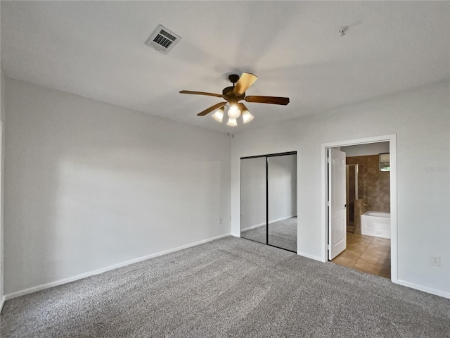 unfurnished bedroom featuring ceiling fan, light colored carpet, ensuite bathroom, and a closet