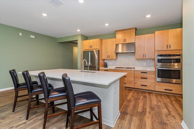 kitchen with stainless steel appliances, sink, hardwood / wood-style flooring, a center island with sink, and a breakfast bar area