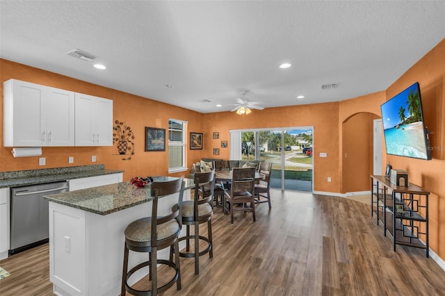 kitchen with ceiling fan, stainless steel dishwasher, hardwood / wood-style floors, dark stone counters, and white cabinets