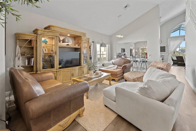 living room with high vaulted ceiling, plenty of natural light, and light wood-type flooring