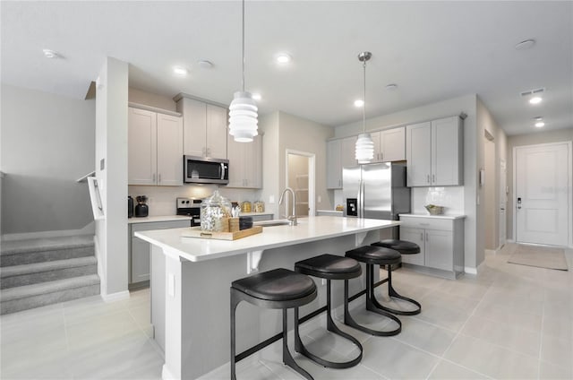 kitchen with sink, hanging light fixtures, light tile patterned floors, an island with sink, and stainless steel appliances