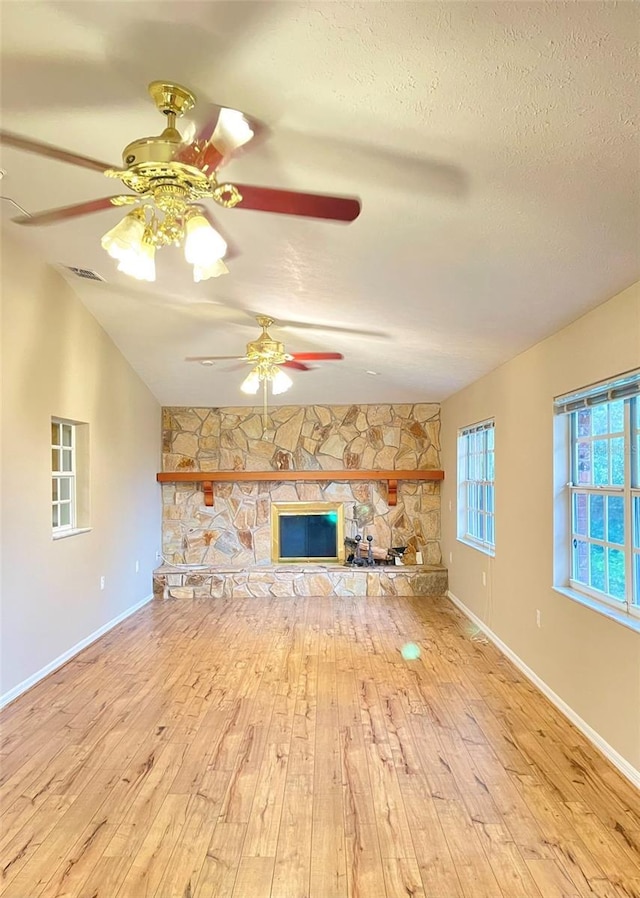 unfurnished living room featuring a textured ceiling, a stone fireplace, light hardwood / wood-style flooring, and lofted ceiling