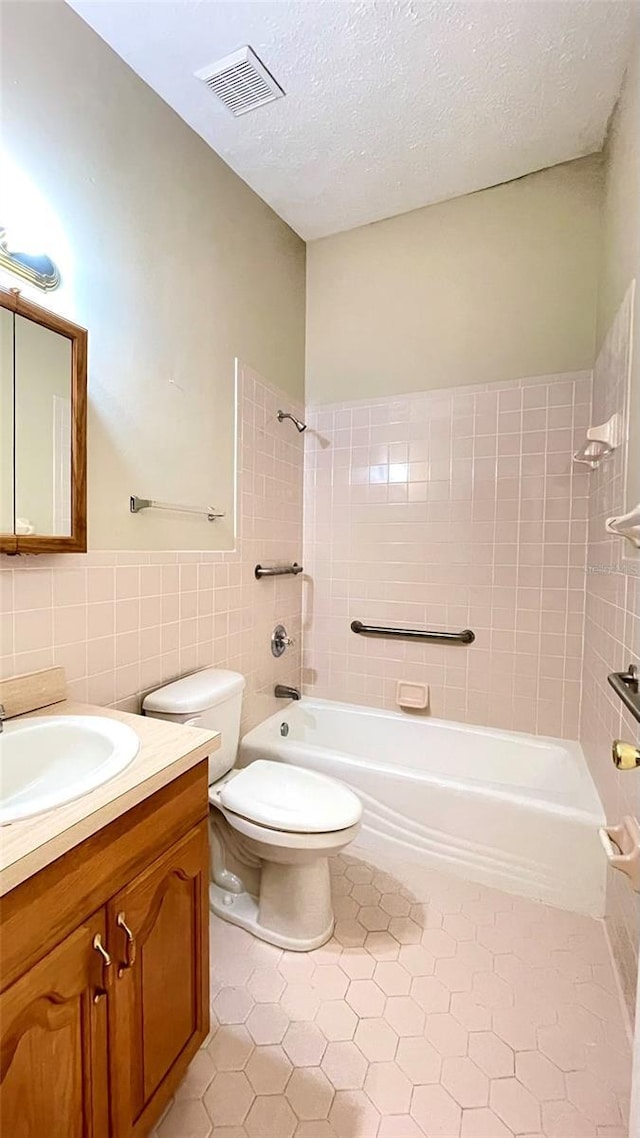 full bathroom featuring a textured ceiling, tiled shower / bath combo, tile walls, tile patterned flooring, and toilet