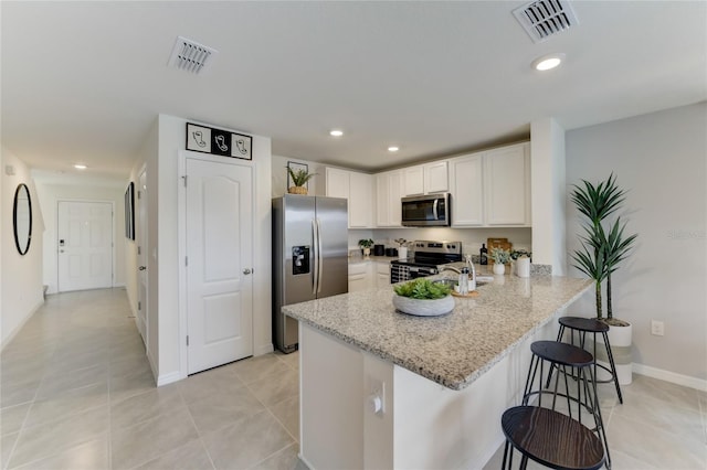 kitchen with white cabinetry, light stone counters, kitchen peninsula, a breakfast bar, and appliances with stainless steel finishes