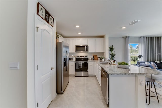 kitchen featuring light stone countertops, appliances with stainless steel finishes, white cabinetry, and a breakfast bar area