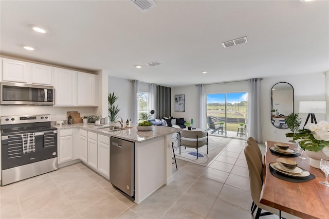 kitchen featuring kitchen peninsula, sink, light tile patterned floors, appliances with stainless steel finishes, and white cabinetry