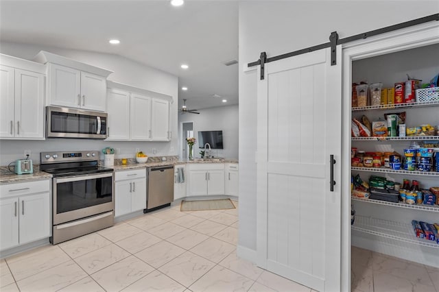 kitchen with white cabinets, a barn door, light stone counters, and appliances with stainless steel finishes