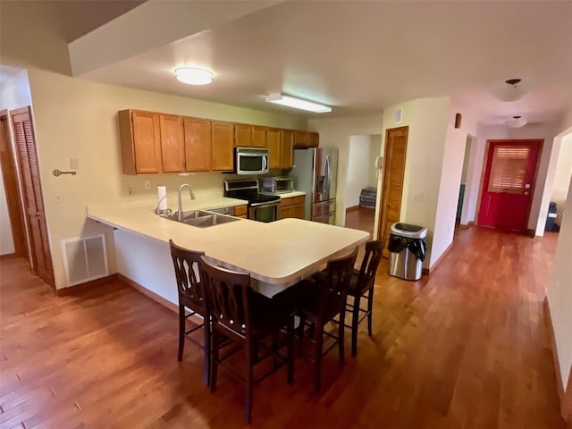 kitchen with hardwood / wood-style floors, kitchen peninsula, sink, a breakfast bar area, and stainless steel appliances