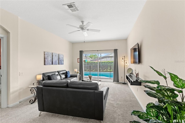 living room featuring ceiling fan, light colored carpet, and a textured ceiling