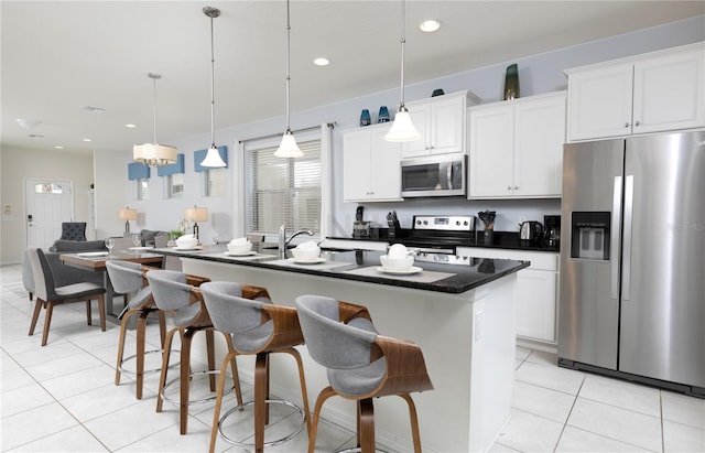 kitchen featuring decorative light fixtures, stainless steel appliances, a kitchen island with sink, and white cabinets