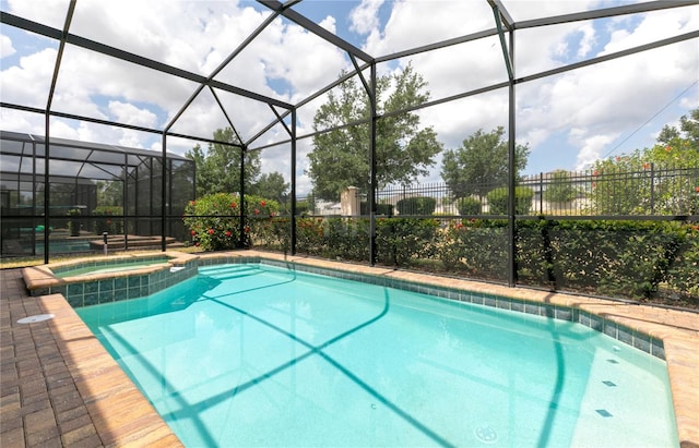 view of pool with a patio area, glass enclosure, and an in ground hot tub