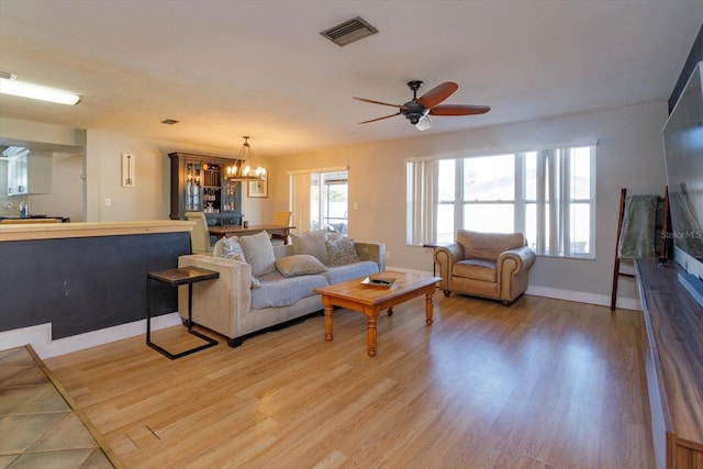 living room with ceiling fan with notable chandelier and light hardwood / wood-style flooring