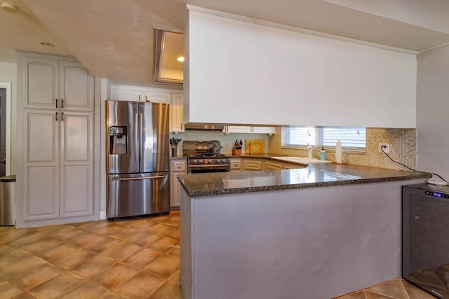 kitchen with white cabinetry, tasteful backsplash, kitchen peninsula, dark stone countertops, and appliances with stainless steel finishes