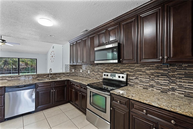 kitchen featuring sink, light stone counters, ceiling fan, dark brown cabinets, and appliances with stainless steel finishes