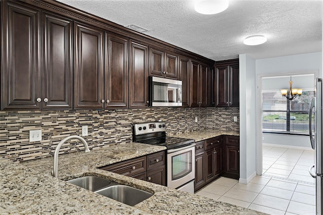 kitchen with stainless steel appliances, light tile patterned flooring, dark brown cabinets, and light stone countertops