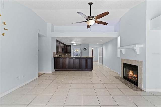 kitchen with a fireplace, ceiling fan, light tile patterned floors, decorative backsplash, and dark brown cabinetry