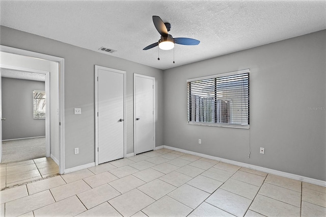 unfurnished bedroom featuring light tile patterned flooring, a textured ceiling, ceiling fan, and multiple windows