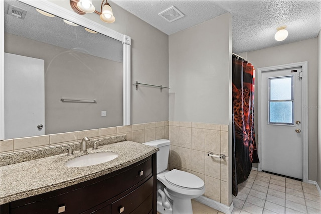 bathroom with toilet, vanity, tile patterned floors, tile walls, and a textured ceiling