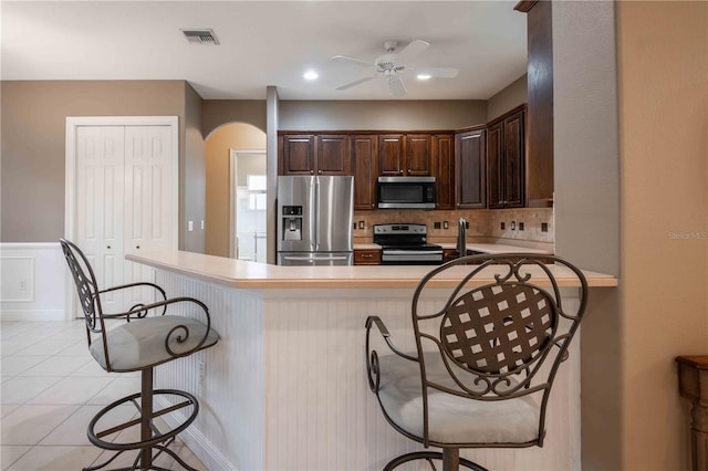 kitchen featuring light tile patterned floors, stainless steel appliances, kitchen peninsula, and a kitchen bar