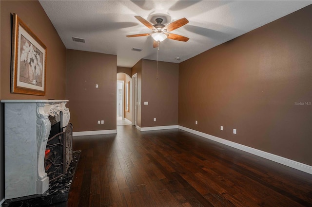 living room with ceiling fan, a high end fireplace, dark hardwood / wood-style floors, and a textured ceiling