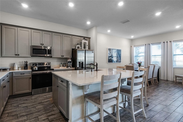 kitchen with gray cabinetry, a center island with sink, stainless steel appliances, and sink