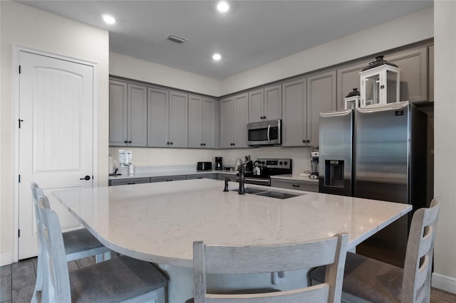 kitchen with sink, light stone counters, stainless steel appliances, and a kitchen island with sink