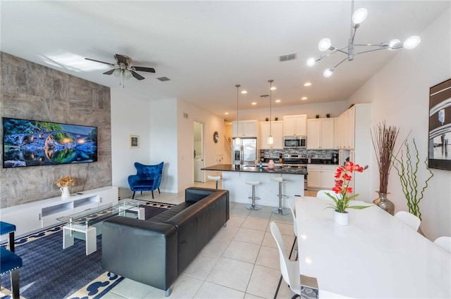 tiled living room with ceiling fan with notable chandelier