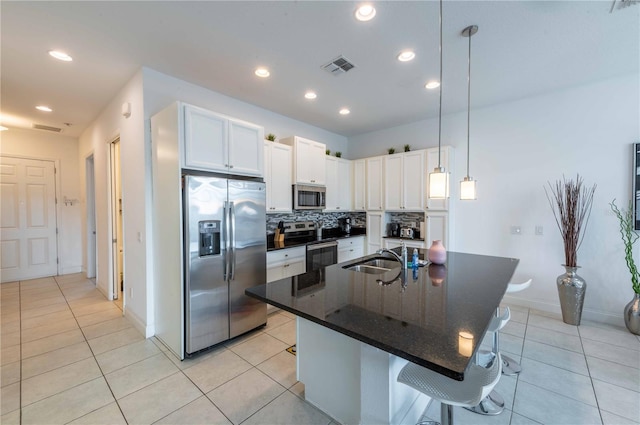 kitchen featuring stainless steel appliances, a kitchen island with sink, sink, white cabinetry, and hanging light fixtures