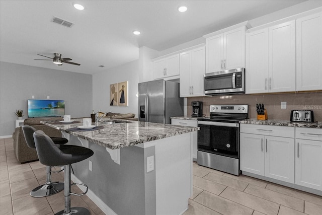 kitchen featuring sink, white cabinets, a center island, light stone countertops, and appliances with stainless steel finishes